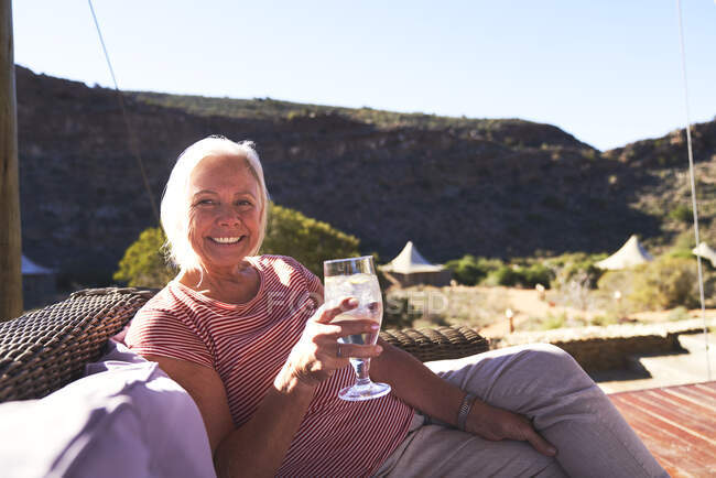 Portrait happy senior woman drinking water on sunny safari hotel patio — Stock Photo