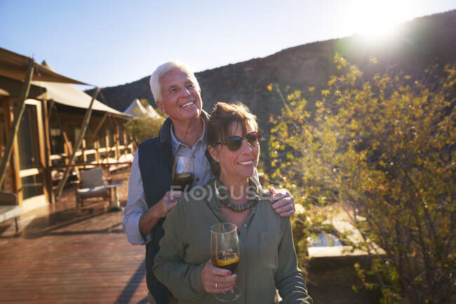 Happy senior couple drinking iced tea on sunny safari lodge balcony — Stock Photo