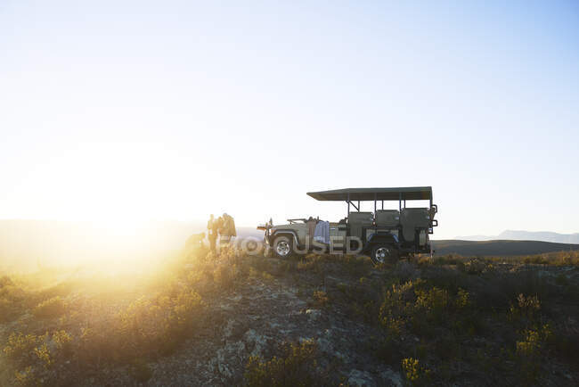 Safari grupo de turismo fora do veículo off-road na colina tranquila ao nascer do sol — Fotografia de Stock