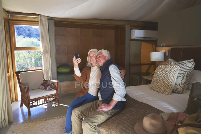 Feliz pareja de ancianos tomando selfie con cámara de teléfono en la habitación del hotel - foto de stock