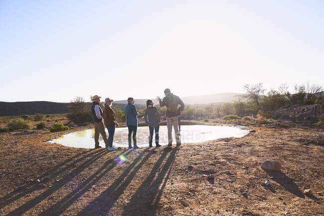 Safari tour guide and group at water in sunny grassland South Africa — Stock Photo