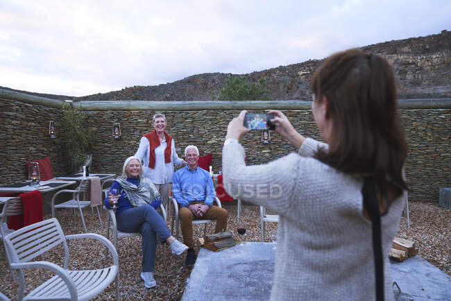 Femme avec appareil photo téléphone photographier des amis âgés sur le patio — Photo de stock
