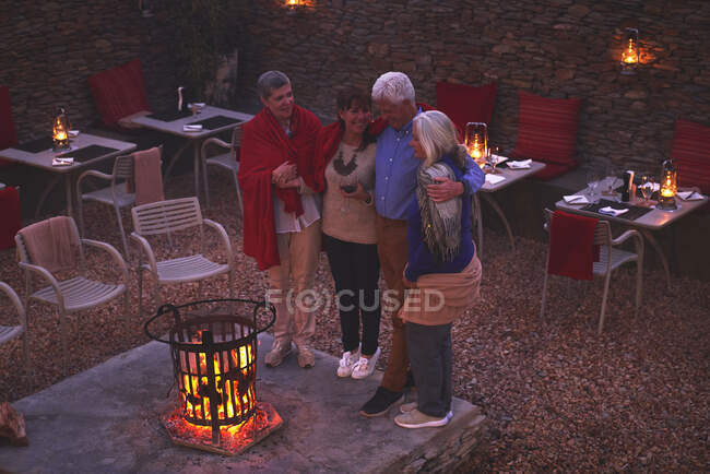 Felices amigos mayores relajándose en el fuego en el patio del hotel - foto de stock