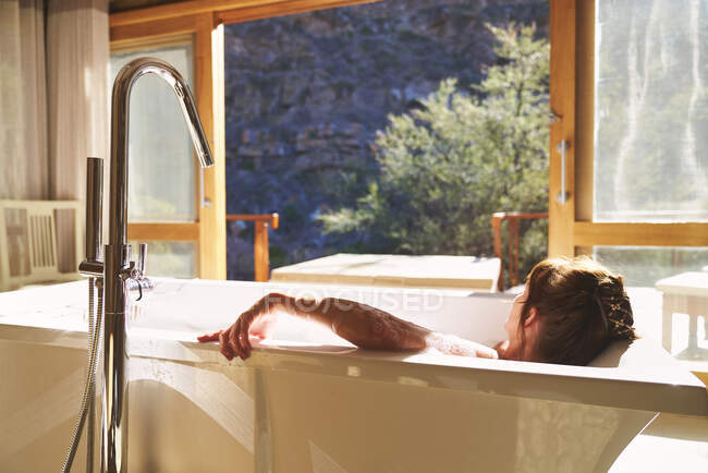 Femme sereine prenant un bain dans une chambre d'hôtel ensoleillée — Photo de stock