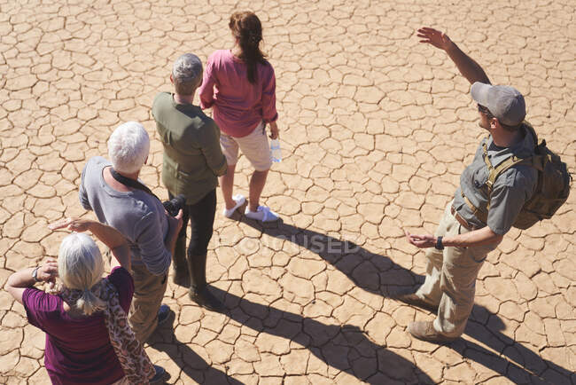 Guia turístico do Safari conversando com grupo na terra ensolarada rachada — Fotografia de Stock