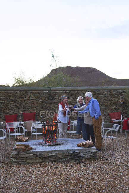 Happy senior friends drinking wine at hotel patio fire pit — Stock Photo