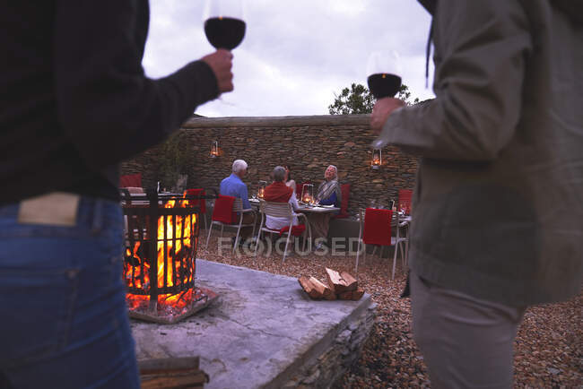 Couple and senior friends dining drinking wine on patio with fire pit — Stock Photo