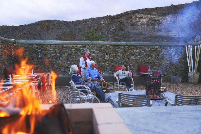 Senior friends relaxing with red wine on hotel patio with fire pit — Stock Photo
