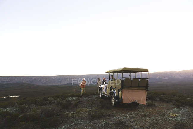 Safari-Reisegruppe und Geländewagen auf abgelegenem Hügel bei Sonnenaufgang — Stockfoto