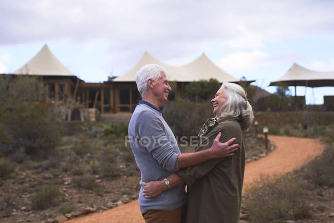 Affectionate senior couple hugging outside safari lodge hotel — Stock Photo