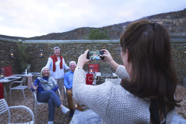Mulher com câmera telefone fotografar amigos seniores no pátio do hotel — Fotografia de Stock