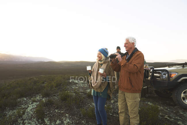 Senior couple on safari using binoculars and drinking tea — Stock Photo
