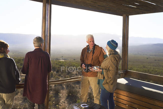 Senior couple with camera and tea on sunny safari lodge balcony — Stock Photo