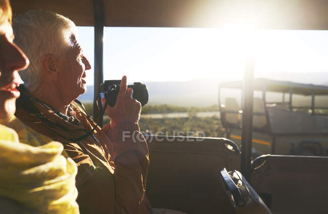 Senior couple with digital camera riding in safari off-road vehicle — Stock Photo