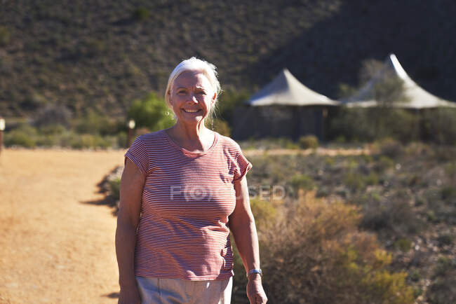 Portrait happy senior woman on sunny footpath outside safari lodge — Stock Photo