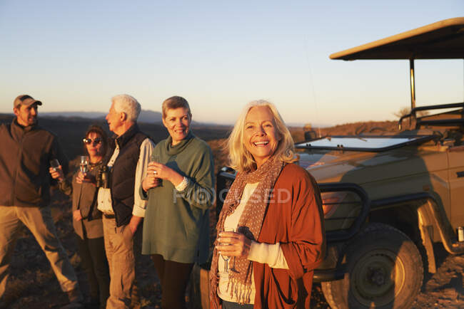 Портрет счастливой пожилой женщины на сафари, пьющей шампанское с друзьями — стоковое фото