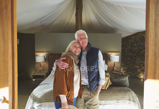 Portrait happy senior couple hugging in safari lodge hotel room — Stock Photo