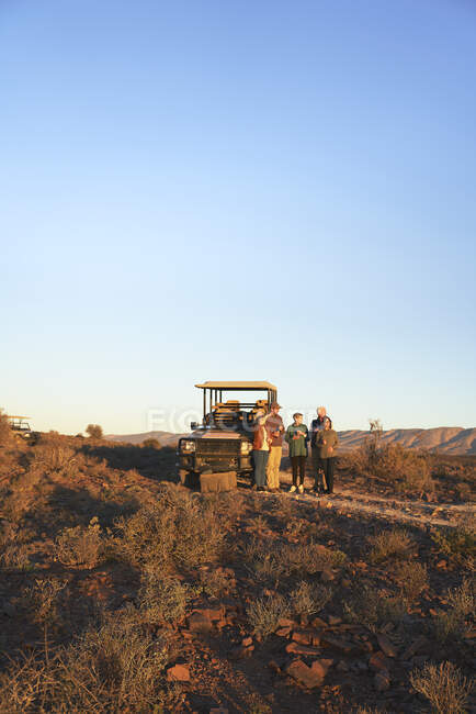 Safari-Reisegruppe steht vor Geländewagen in sonnigem Grasland — Stockfoto