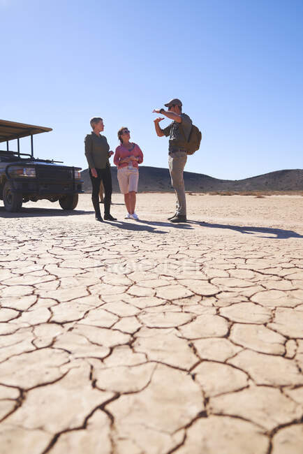 Safari guida turistica parlando con la coppia nel soleggiato deserto arido — Foto stock