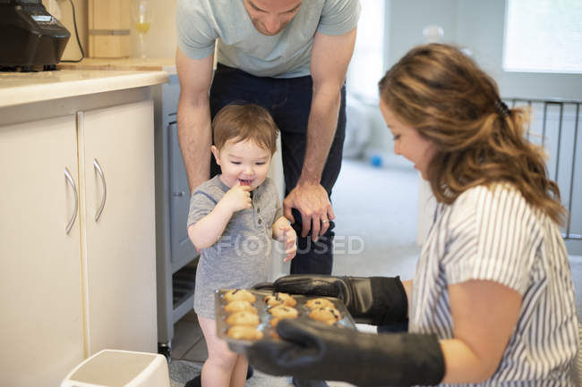 Menina criança curiosa assistindo mãe assar muffins na cozinha — Fotografia de Stock