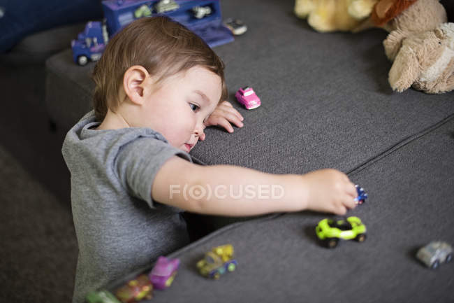 Любопытная милая малышка играет с игрушечными машинками на диване — стоковое фото
