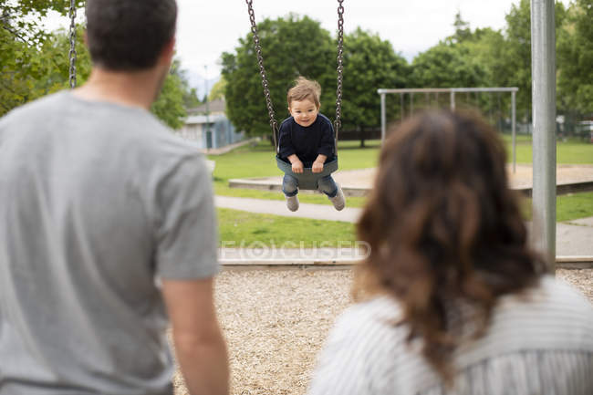 Parents watching carefree toddler girl swinging at playground — Stock Photo