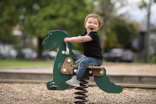 Безтурботна мила дівчинка, що катається на іграшці динозавра на дитячому майданчику — стокове фото