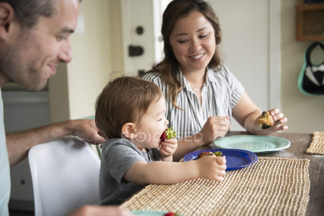 Parents watching cute toddler daughter eating strawberry — Stock Photo