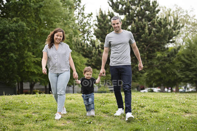 Портрет щасливої молодої сім'ї, що йде в парковій траві — стокове фото