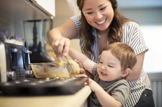 Happy mother and toddler daughter baking muffins in kitchen — Stock Photo