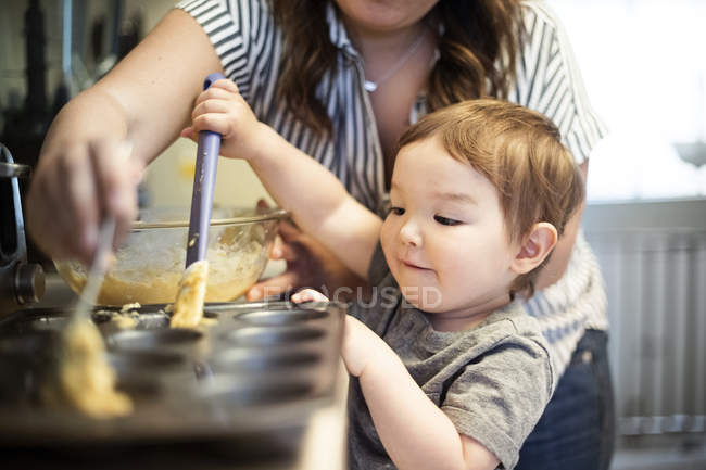 Linda niña hornear magdalenas con madre - foto de stock