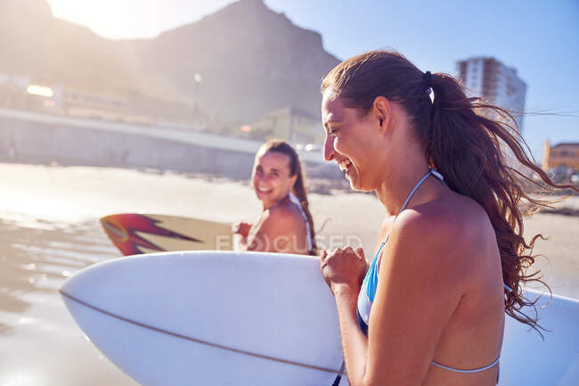 Jovens amigas felizes com pranchas de surf na praia ensolarada — Fotografia de Stock