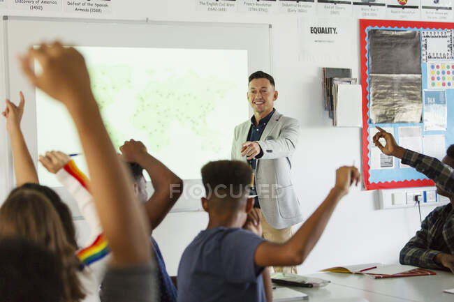 High school teacher leading lesson, calling on students with arms raised in classroom — Stock Photo