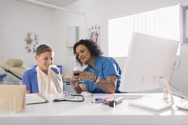 Pediatra mujer recetando medicamentos para niño con el brazo en honda en el consultorio médico - foto de stock
