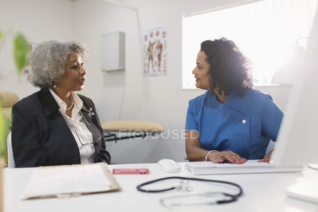 Жіночий лікар, який розмовляє зі старшою пацієнткою за комп 