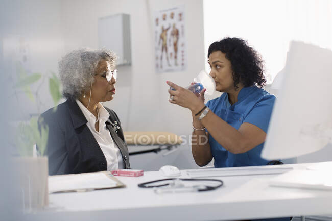 Médica do sexo feminino ensinando paciente sênior como usar inalador em consultório médico — Fotografia de Stock