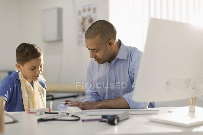 Male pediatrician showing digital x-ray to boy with arm in sling in doctors office — Stock Photo