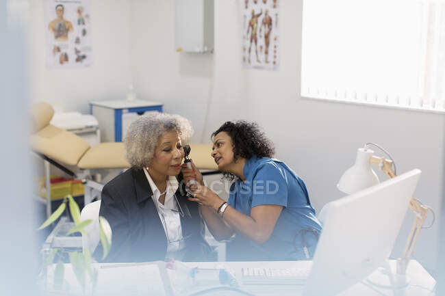 Female doctor examining ear of senior patient with otoscope in doctors office — Stock Photo