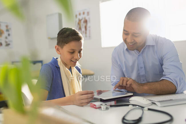 Male pediatrician showing digital tablet to boy patient in doctors office — Stock Photo