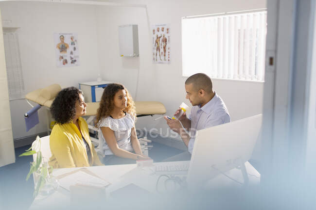 Male pediatrician showing girl patient how to use inhaler in doctors office — Stock Photo