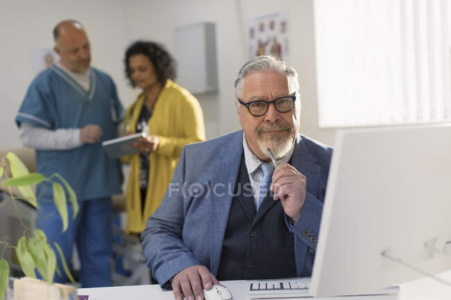 Retrato confiado médico varón que trabaja en la computadora en la oficina de médicos - foto de stock