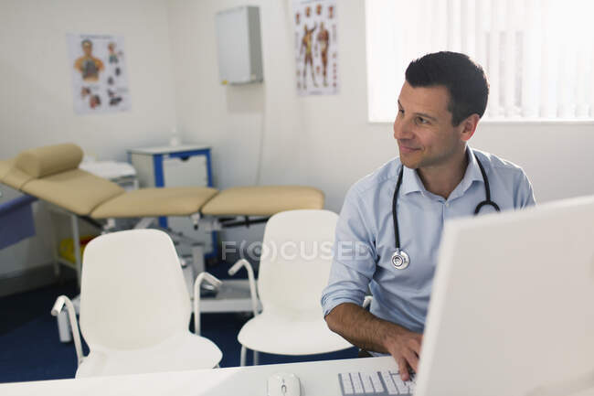 Confident male doctor working at computer in doctors office — Stock Photo