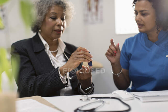 Жінка-лікар, яка викладає діабетичний старший пацієнт як використовувати глюкометр — стокове фото