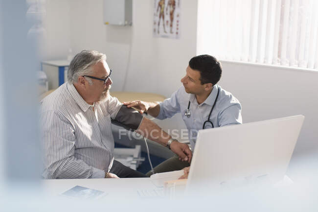 Чоловік-лікар перевіряє артеріальний тиск пацієнта в кабінеті лікарів — стокове фото