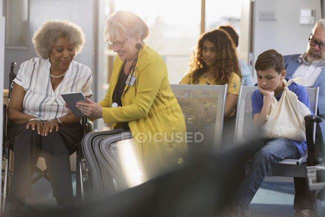 Female doctor with digital tablet talking to patient in clinic lobby — Stock Photo