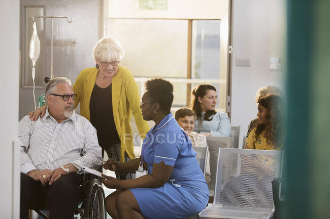 Enfermera hablando con paciente mayor en silla de ruedas en el vestíbulo de la clínica - foto de stock