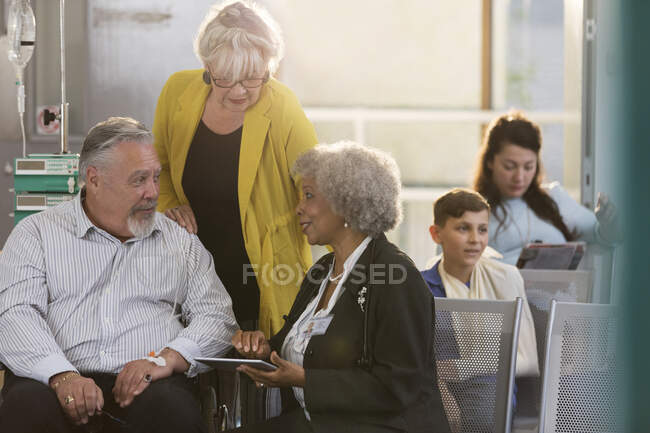 Ärztin mit digitalem Tablet im Gespräch mit Senioren-Paar in Klinik-Lobby — Stockfoto