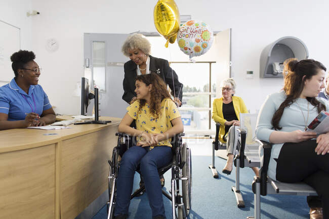 Mujer recepcionista saludo niña paciente en silla de ruedas en la clínica - foto de stock