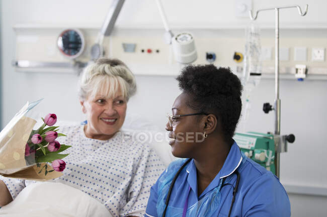 Жінка-пацієнтка, що показує квіти доглядати в лікарняній кімнаті — стокове фото