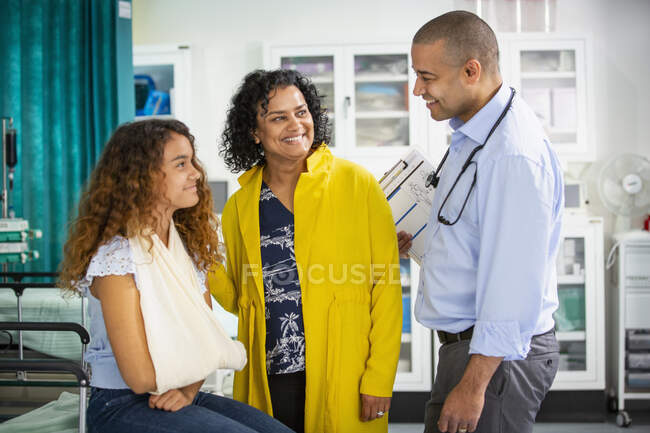 Pediatra do sexo masculino conversando com paciente menina com braço na funda na sala de exame — Fotografia de Stock